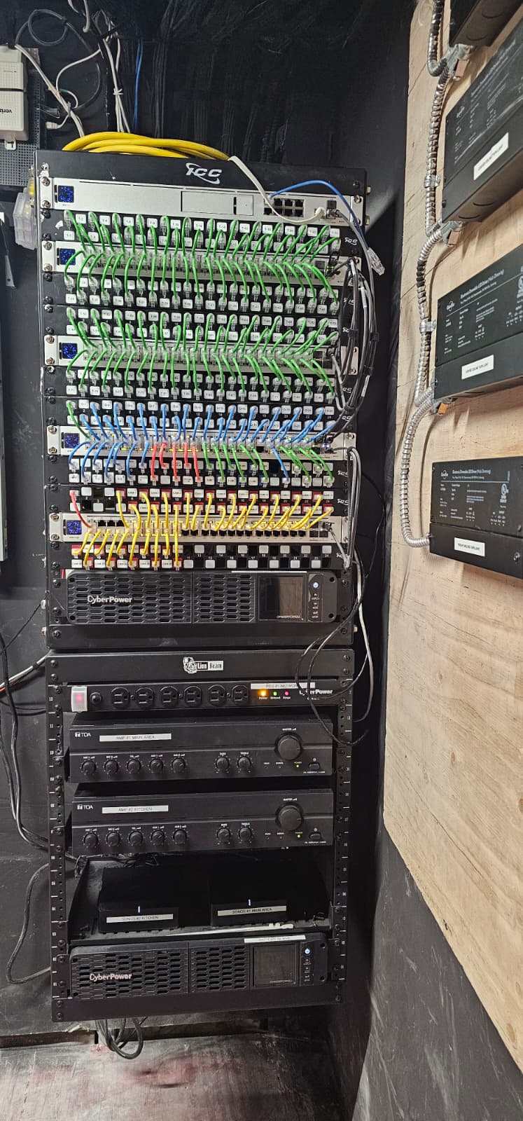 Finished rack with color-coded patch cabling, managed switches, audio amplifiers, and dual UPS units