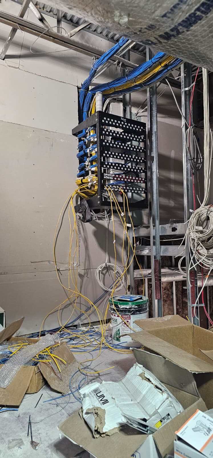 Wall-mounted rack during rough-in with cable bundles arriving and patch panels being terminated